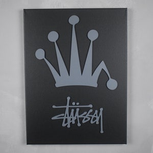 May include: A black canvas painting with a gray crown and the word "Stussy" in a stylized font.