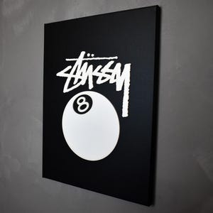 May include: A black canvas print with a white 8-ball and the word "STUSSY" in white lettering.
