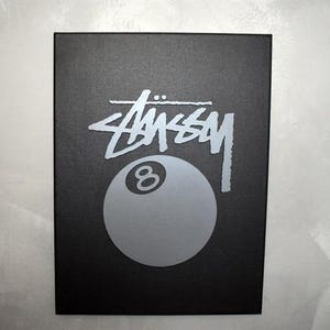 May include: Black box with a silver 8-ball and the word "STUSSY" in silver lettering.