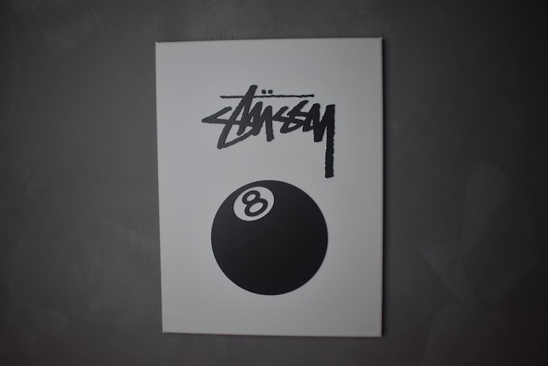 May include: White canvas print with a black and white graphic of the Stussy logo and a black 8-ball.