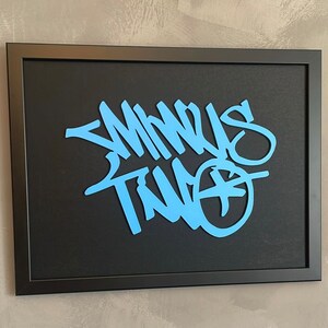 May include: A black framed artwork with a blue and white graffiti-style design that says "Minus Two".