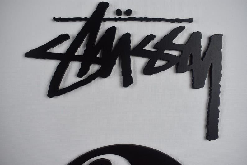 May include: Black and white logo of the brand "Stussy" with a stylized font. The logo is on a white background.