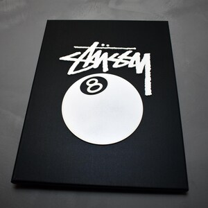 May include: Black and white graphic of a 8-ball with the word "STUSSY" in white lettering on a black background.