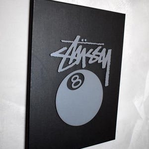 May include: A black canvas print with a gray 8-ball and the word "STUSSY" in a stylized font.