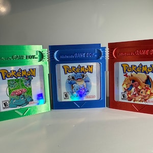 Op de afbeelding: Drie Nintendo Game Boy-cartridges voor het Pokémon-videospel. De cartridges zijn groen, blauw en rood. Elke cartridge heeft een ander Pokémon-personage op de voorkant.