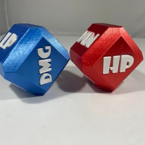 Peut inclure: Deux dés, l'un bleu et l'autre rouge, avec des lettres blanches. Le dé bleu porte les inscriptions "DMG" et "LP". Le dé rouge porte les inscriptions "HP" et "WIN".