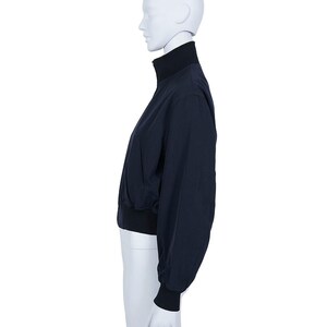 May include: A navy blue jacket with a high, black collar and black cuffs. The jacket has a full-length zip and a fitted waist. The sleeves are long and slightly puffed. The jacket is displayed on a white mannequin.