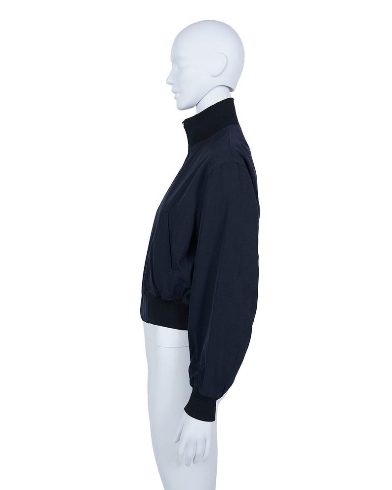 May include: A navy blue jacket with a high, black collar and black cuffs. The jacket has a full-length zip and a fitted waist. The sleeves are long and slightly puffed. The jacket is displayed on a white mannequin.