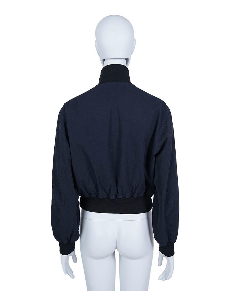 May include: Navy blue bomber jacket with a black collar, cuffs, and waistband, displayed on a mannequin. The back view showcases the jacket's design and fit. A casual outerwear piece, suitable for various occasions.