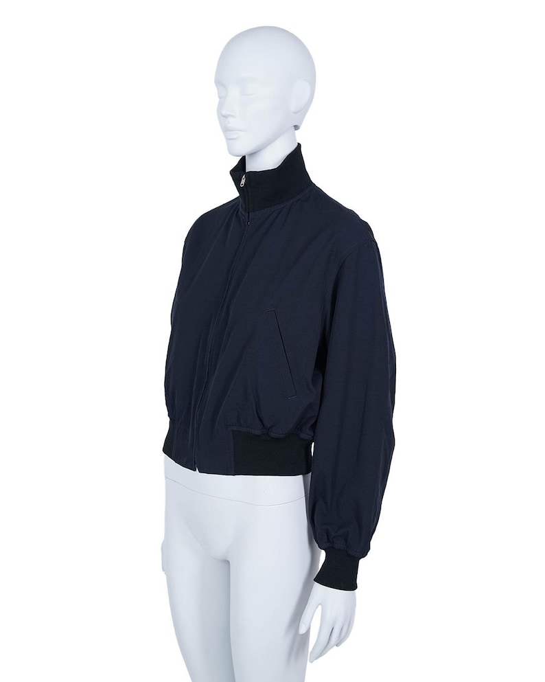 May include: A navy blue bomber jacket with a black collar, cuffs, and waistband. The jacket features a front zip and a relaxed fit. The long sleeves are slightly gathered at the cuffs. The jacket is displayed on a mannequin.