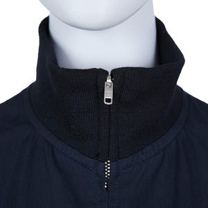 May include: A close-up shot of a navy blue jacket featuring a black ribbed collar and a silver zipper. The jacket is presented on a mannequin, highlighting the design and details of the garment.