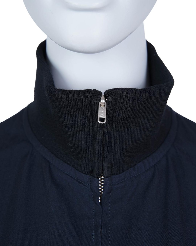 May include: A close-up shot of a navy blue jacket featuring a black ribbed collar and a silver zipper. The jacket is presented on a mannequin, highlighting the design and details of the garment.