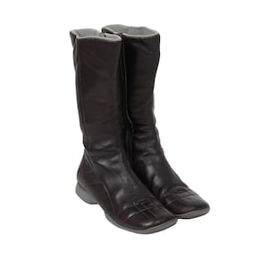 May include: A pair of dark brown mid-calf boots featuring a square toe design with a grid-like stitched pattern on the vamp. The boots have a side zipper closure, a light gray interior lining, and a flat, light gray rubberized outsole.