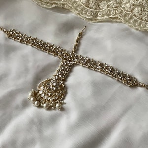 May include: A gold and white jeweled headpiece with a large round pendant and pearl accents.