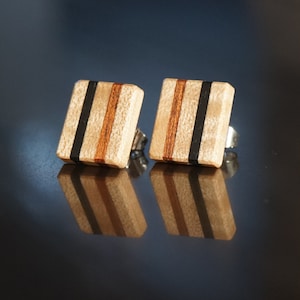 May include: A pair of square wooden earrings with black and brown stripes. The earrings have silver posts.