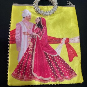 May include: Yellow clutch with a silver beaded handle. The clutch features a printed image of a couple in traditional wedding attire. The couple is standing in front of a red and white backdrop. The clutch has a gold zipper and trim.