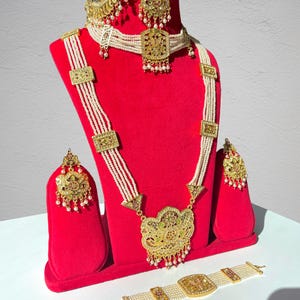 May include: A traditional Indian bridal jewelry set with a gold necklace, earrings, and a bracelet. The necklace features multiple strands of white pearls and intricate gold pendants. The earrings and bracelet also have gold accents and pearl details.
