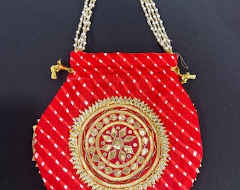 May include: A red fabric pouch with a white diagonal stripe pattern. The pouch features a gold and silver embroidered circular design in the center and a beaded handle. The pouch is approximately 6 inches wide.
