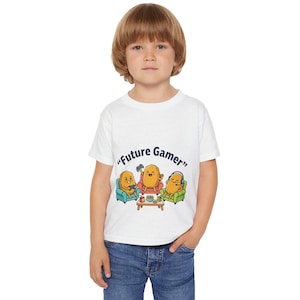 Op de afbeelding: Wit t-shirt met de tekst "Future Gamer" en een illustratie van drie aardappelpersonages die videogames spelen. De aardappels zitten in fauteuils, een met een controller, een met een koptelefoon, en een kleine tafel.
