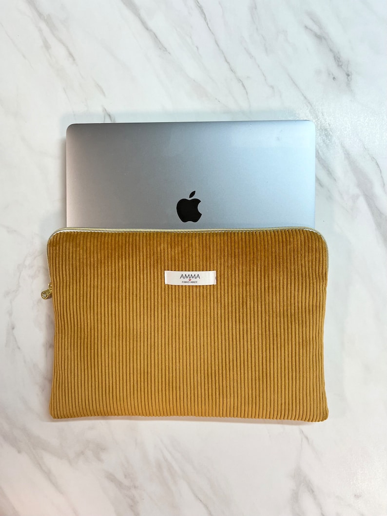 Housse d'ordinateur Velours Côtelé Moutarde - Résistante & Douce - Dispo IPad et tablette.
Un macbook pro Apple dépasse de la pochette