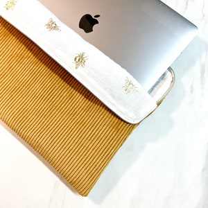 Housse d'ordinateur Velours Côtelé Moutarde et sa doublure double gaze de coton abeilles dorées - Résistante & Douce - Dispo IPad et tablette.
Un macbook pro Apple dépasse de la pochette