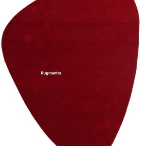 May include: A solid red, irregularly shaped rug with a slightly pointed bottom. The rug is made of a soft, plush material. The text "Rugmantra" is printed in white in the center of the rug.