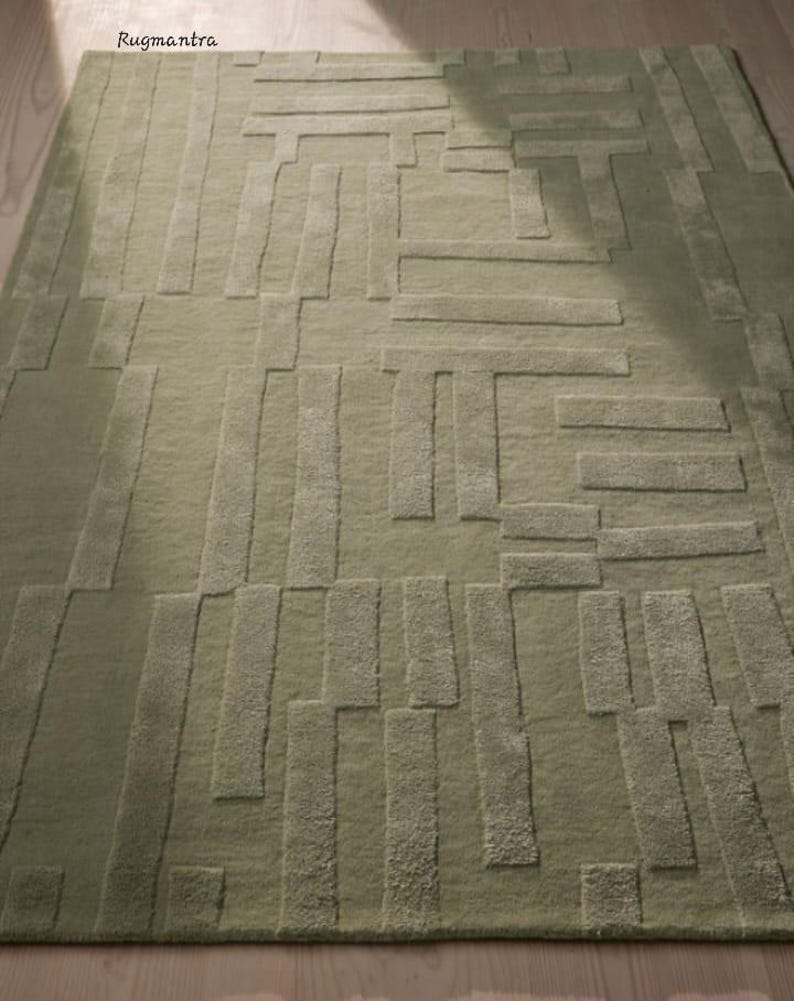 May include: A green area rug with a geometric pattern of raised lines and rectangles. The rug has a subtle texture and a contemporary design.