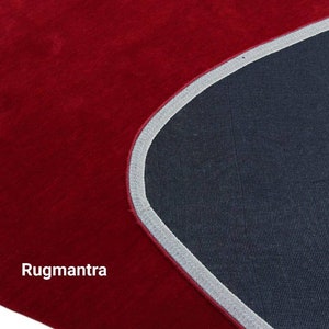 May include: Close-up of a red rug with a gray border. The rug is made of a soft, plush material. The text "Rugmantra" is visible in the lower left corner of the image.