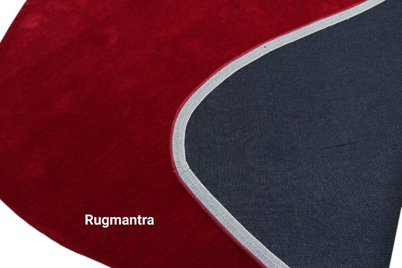 May include: Close-up of a red rug with a gray border. The rug is made of a soft, plush material. The text "Rugmantra" is visible in the lower left corner of the image.