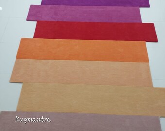May include: A set of seven colorful runner rugs in shades of purple, pink, red, orange, beige, and brown. The rugs are arranged in a stack, with the purple rug on top and the brown rug on the bottom. The rugs are all made of a soft, plush material.