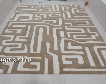 May include: A large, abstract area rug with a geometric pattern in shades of beige and white. The rug has a rounded edge and the text "Rugmantra" is visible in the lower left corner.