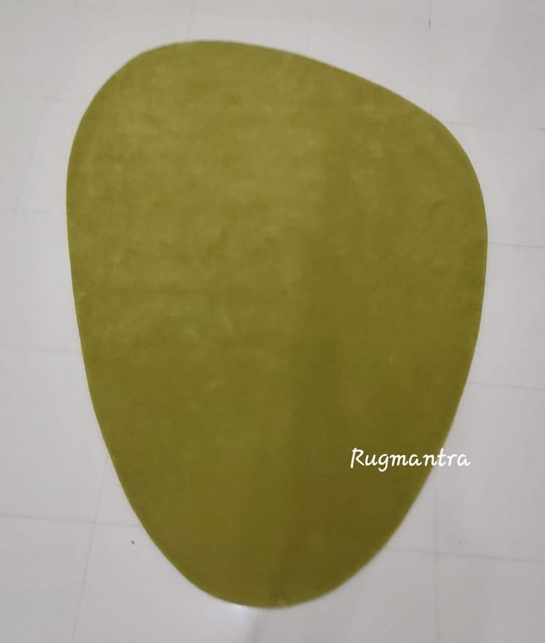 May include: A large, green, oval-shaped rug with a smooth texture. The rug is on a white tiled floor. The text "Rugmantra" is visible in the lower right corner of the rug.