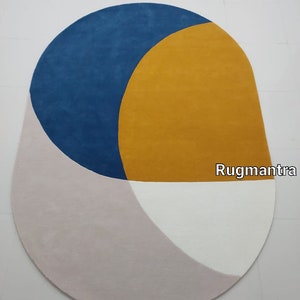 May include: A modern oval rug with geometric shapes in shades of blue, yellow, pink, and white. The rug has a contemporary design and is perfect for adding a touch of color and style to any room.