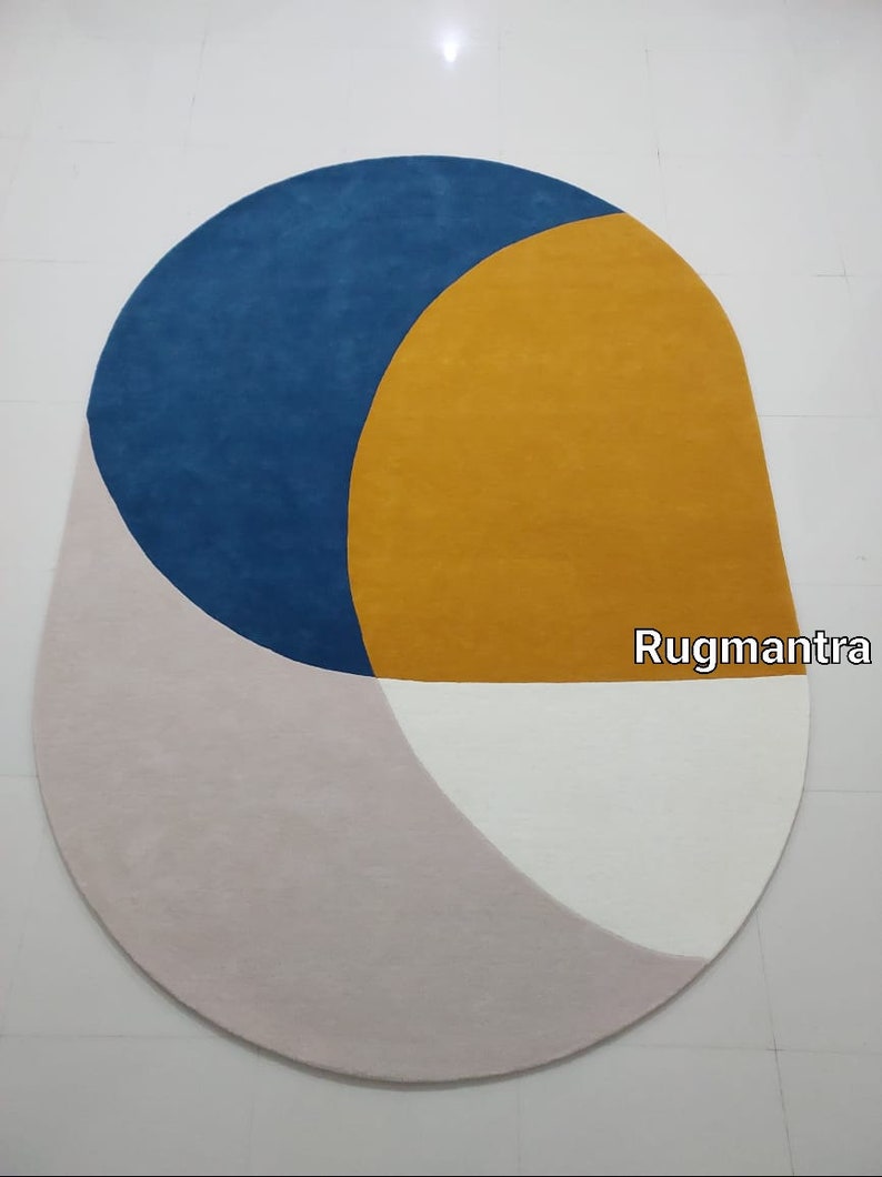 May include: A modern oval rug with geometric shapes in shades of blue, yellow, pink, and white. The rug has a contemporary design and is perfect for adding a touch of color and style to any room.