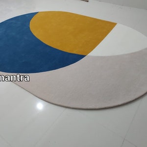 May include: A round, multi-colored rug with a blue, yellow, white, and gray geometric design. The rug is made of soft, plush material.