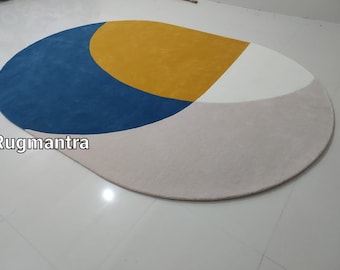 Puede incluir: Una alfombra redonda multicolor con un diseño geométrico azul, amarillo, blanco y gris. La alfombra está hecha de un material suave y mullido.