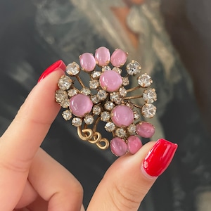 May include: A vintage brooch with a cluster of pink and clear rhinestones. The brooch is made of gold-toned metal and has a delicate, floral design.