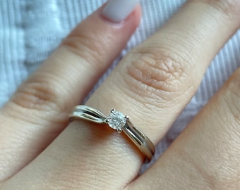 Könnte beinhalten: Ein silberner Ring mit einem einzigen, runden, klaren Diamanten, der in der Mitte sitzt. Der Ring hat ein verdrehtes Band.