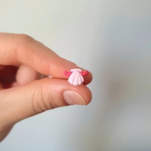 Può includere: Un piccolo ciondolo a forma di conchiglia rosa con accenti rossi. Il ciondolo è piccolo e delicato, perfetto per aggiungere un tocco di fantasia a gioielli o artigianato.