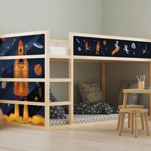 May include: A wooden bunk bed with space-themed panels. The panels depict rockets, planets, and astronauts against a dark blue starry backdrop. The bed has a lower sleeping area, a ladder, and a small table with a stool.