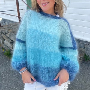 May include: A light blue, fuzzy knit jumper with a gradient pattern. The jumper has a relaxed fit and long sleeves.