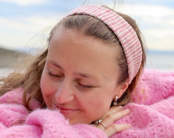 May include: A woman with long brown hair wearing a pink and white striped headband and a pink fuzzy sweater. She is smiling and looking down.