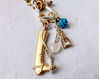 May include: Gold-toned charm bracelet featuring a cowboy boot, stirrup, and turquoise rose charms. The bracelet has a gold and silver chain with a lobster clasp. A heart-shaped charm is also included.
