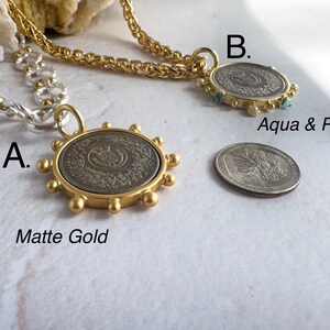 May include: Two gold necklaces with coin pendants. The first necklace is a silver chain with a matte gold coin pendant. The second necklace is a gold chain with a gold coin pendant with aqua and pearl accents. The text "A. Matte Gold" and "B. Aqua & Pearl" is visible below the pendants.