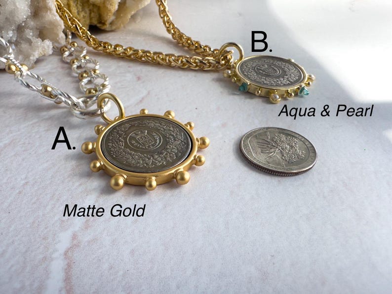 May include: Two gold necklaces with coin pendants. The first necklace is a silver chain with a matte gold coin pendant. The second necklace is a gold chain with a gold coin pendant with aqua and pearl accents. The text "A. Matte Gold" and "B. Aqua & Pearl" is visible below the pendants.