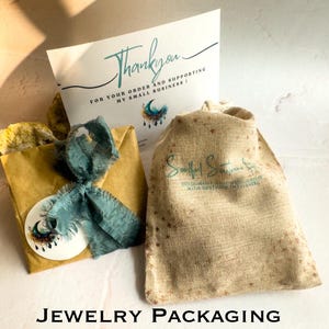 May include: A brown paper bag with a blue ribbon and a sticker with a moon and stars design. The bag is sitting on a white surface next to a burlap bag with a logo that says "Soulful Siren" and a thank you card that says "Thank you for your order and supporting my small business!"