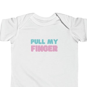Puede incluir: Un body blanco para bebé con el texto "PULL MY FINGER" en letras azules y rosas.