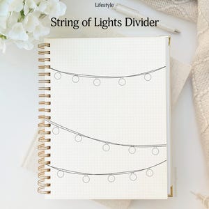 May include: A spiral-bound notebook with a dot grid pattern. The cover features the text "String of Lights Divider" and a simple line drawing of string lights. A pen and decorative elements are in the background.