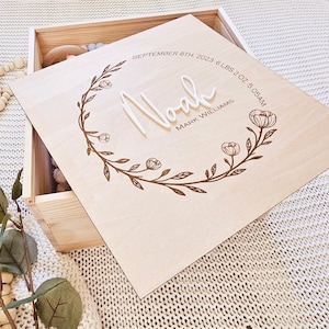 May include: A wooden keepsake box with a floral design and the inscription "Noah Mark Williams September 8th, 2023 6 lbs 2 oz 5:05 AM!"