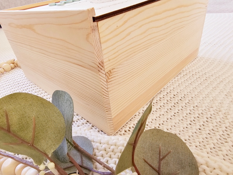 May include: A wooden box with a natural wood finish. The box is closed and the lid is slightly ajar. The box is sitting on a white knitted surface.